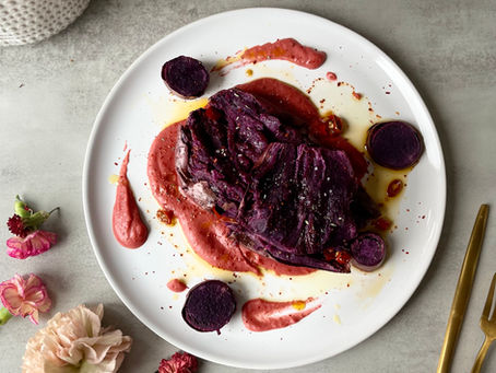 A vibrant Valentine’s Day dish of roasted purple sweet potatoes on a bed of creamy pickled beet hummus, topped with melted butter and sliced marinated chilies, plated elegantly for an intimate dinner or special occasion.