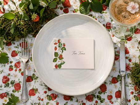 a strawberry place card lays flat on a white dinner plate on a strawberry garden themed outdoor garden party table