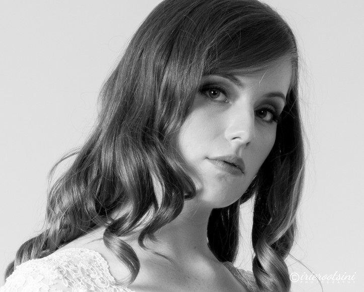 A woman with long hair poses elegantly in a white dress for a modelling headshot.