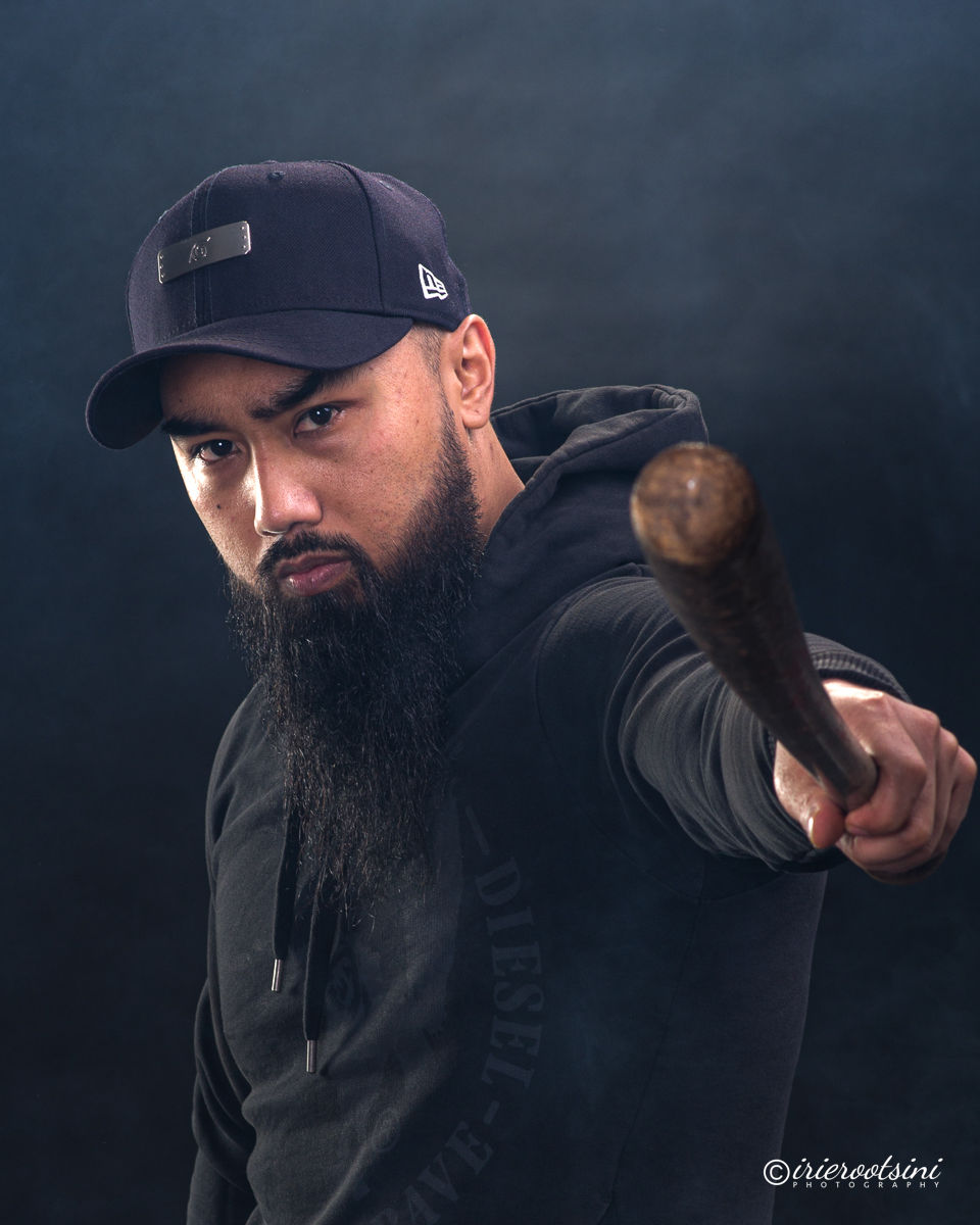 Dramatic acting pose with beard, cap and bat, intense stare toward camera