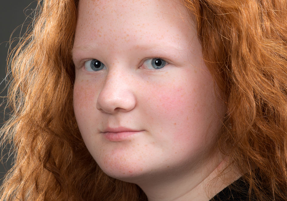 A woman with red hair wearing a black shirt poses for a studio headshot, showcasing her confident expression.