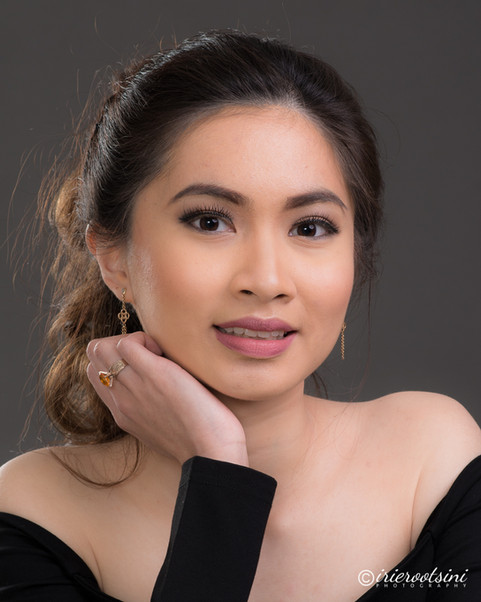 A woman with dark hair poses elegantly in a black dress, showcasing her modelling talent in a professional headshot.