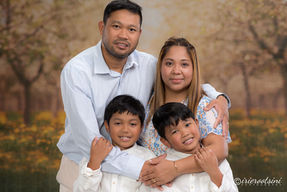 Studio portrait of parents embracing their two young sons against an outdoor-themed backdrop.