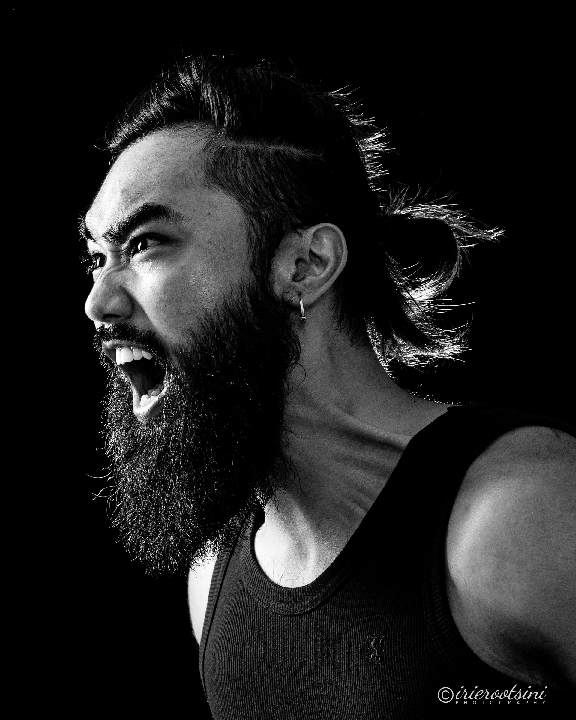 Black and white studio portrait of male actor shouting, captured with Rembrandt lighting for dramatic effect.