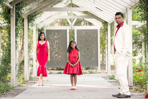 Parents watching their young daughter walk between them during an outdoor portrait session.