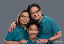 Studio portrait of parents in matching teal shirts, embracing their young son.