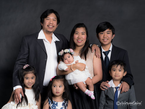 Parents with five young children, including a baby girl, gathered for a joyful studio portrait.