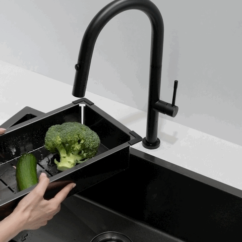 A person holds a black colander with a vegetable over a double sink, demonstrating the spray function of black gooseneck kitchen tapware.