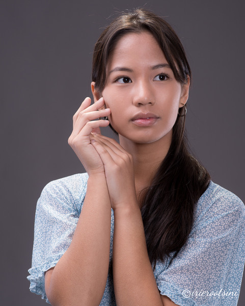 A young woman poses for a modelling headshot, gently holding her hand to her face with a thoughtful expression.