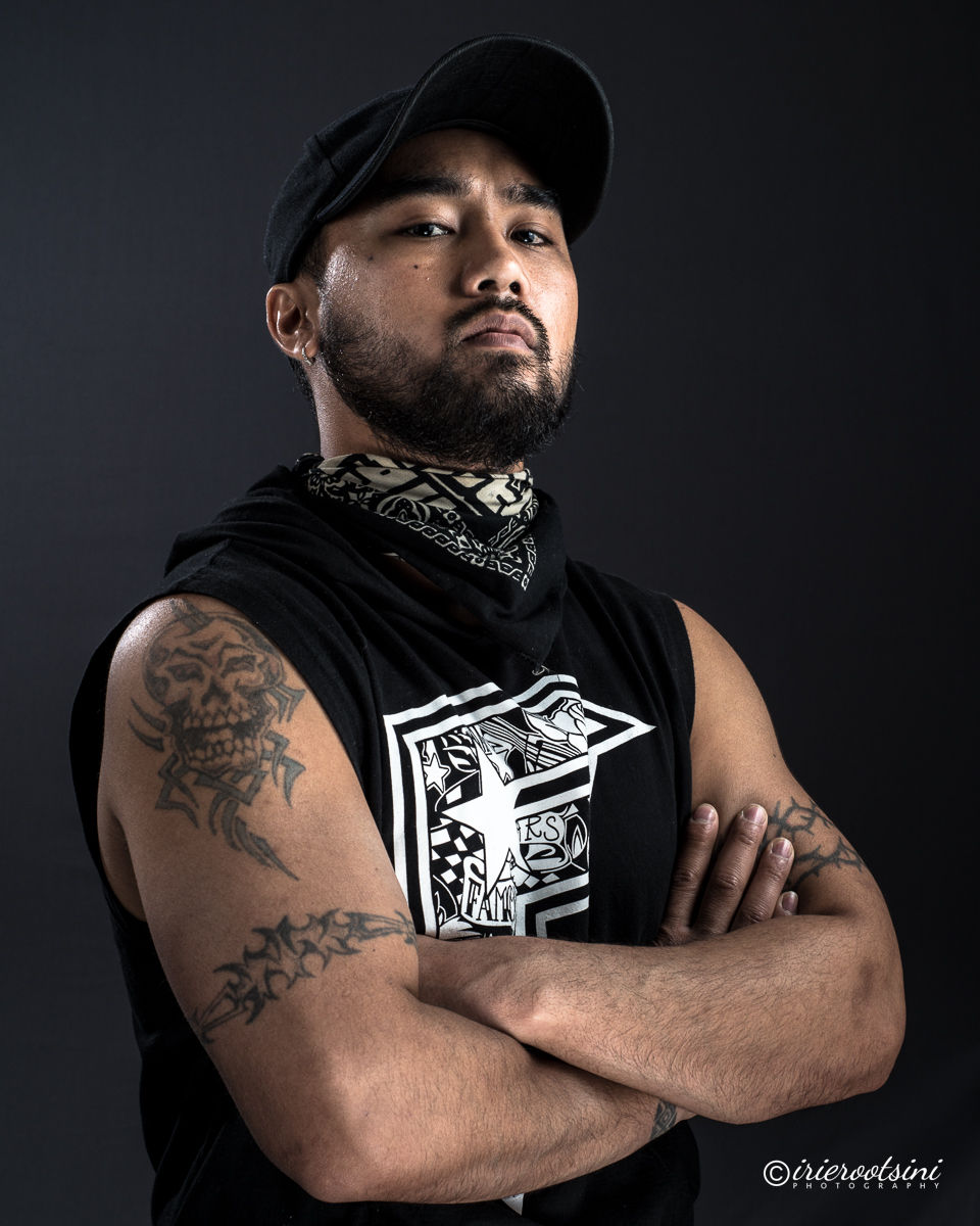 Strong headshot pose with cap and sleeveless shirt, arms crossed