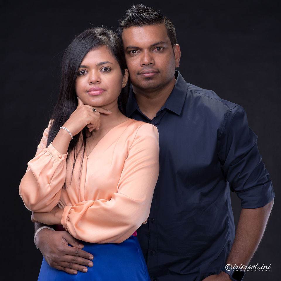 Studio couples portrait of woman in peach blouse and man in navy shirt with black backdrop