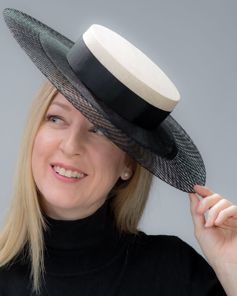 Editorial portrait of Bec Bayss, a blonde woman wearing a wide-brimmed black and white hat with a natural smile, photographed against a neutral grey backdrop for publication in The Hat Magazine, Issue #82.