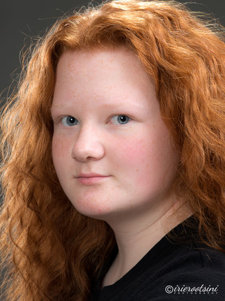 Teen female actor headshot in black top, neutral confident expression, direct eye contact.
