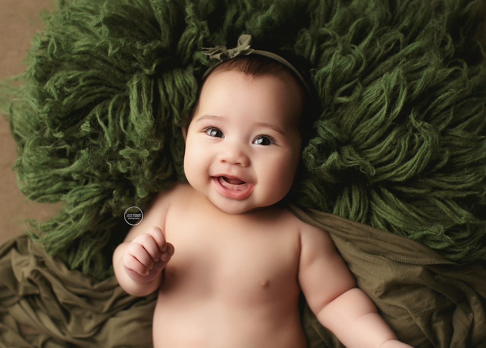 newborn baby girl professional portrait laying on olive green prop smiling