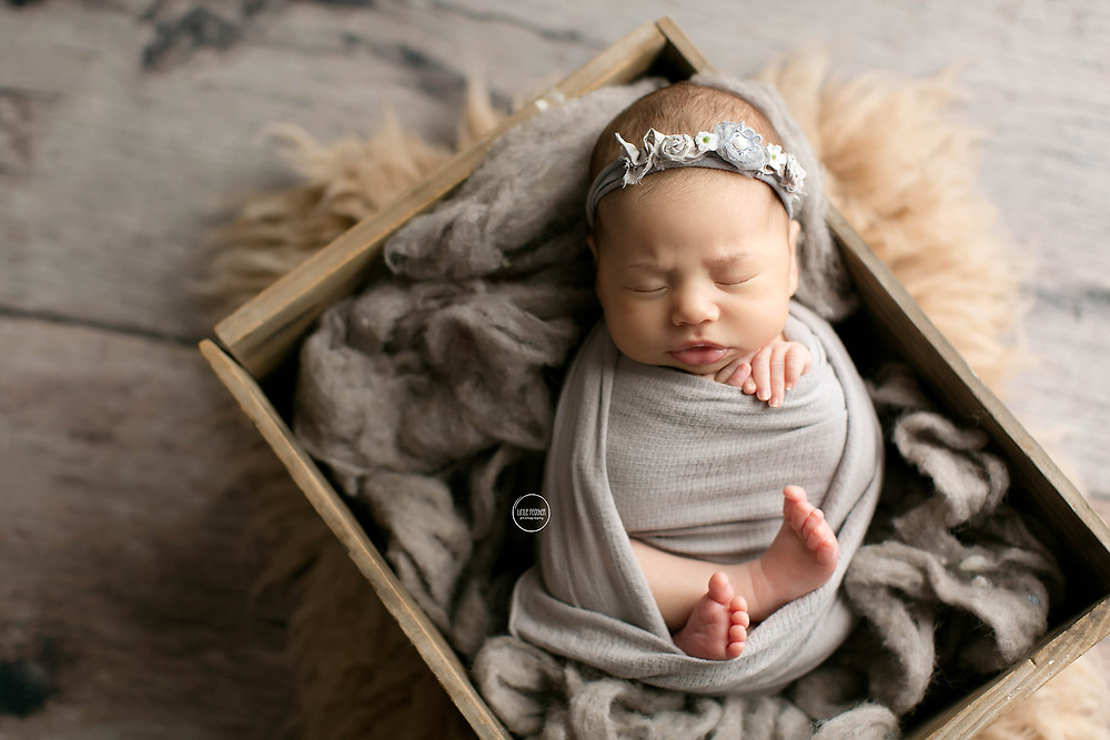 sleeping newborn baby in grey headband and wrap inside a rustic box