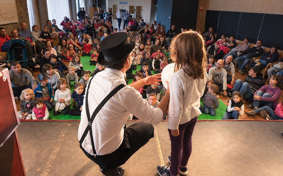 El mag Eduard Juanola, d’esquenes, fent un joc de màgia amb un globus amb una nena en un acte públic a Barcelona