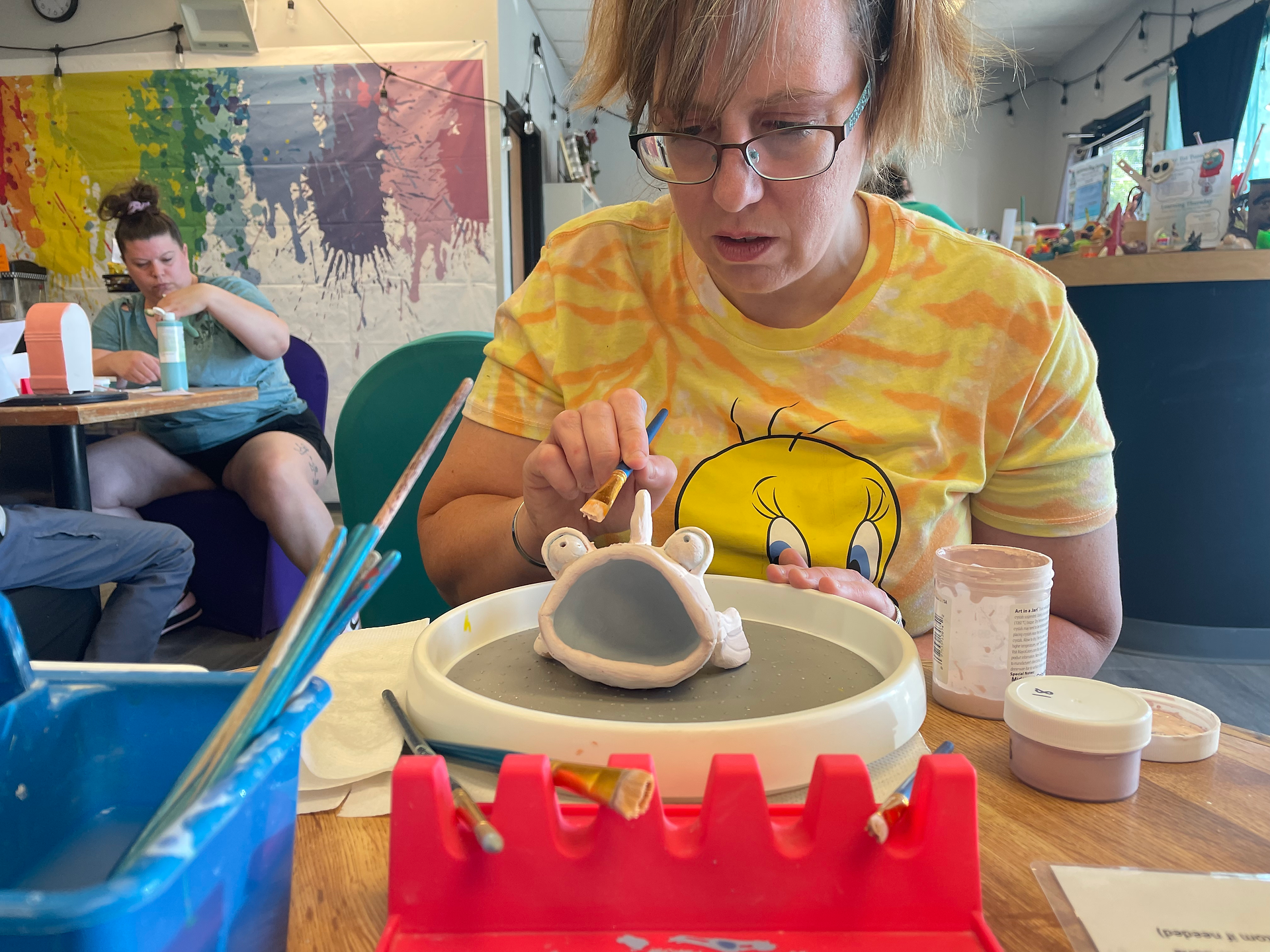 Woman in yellow Tweedy Bird t-shirt painting a clay fish on a round turn table