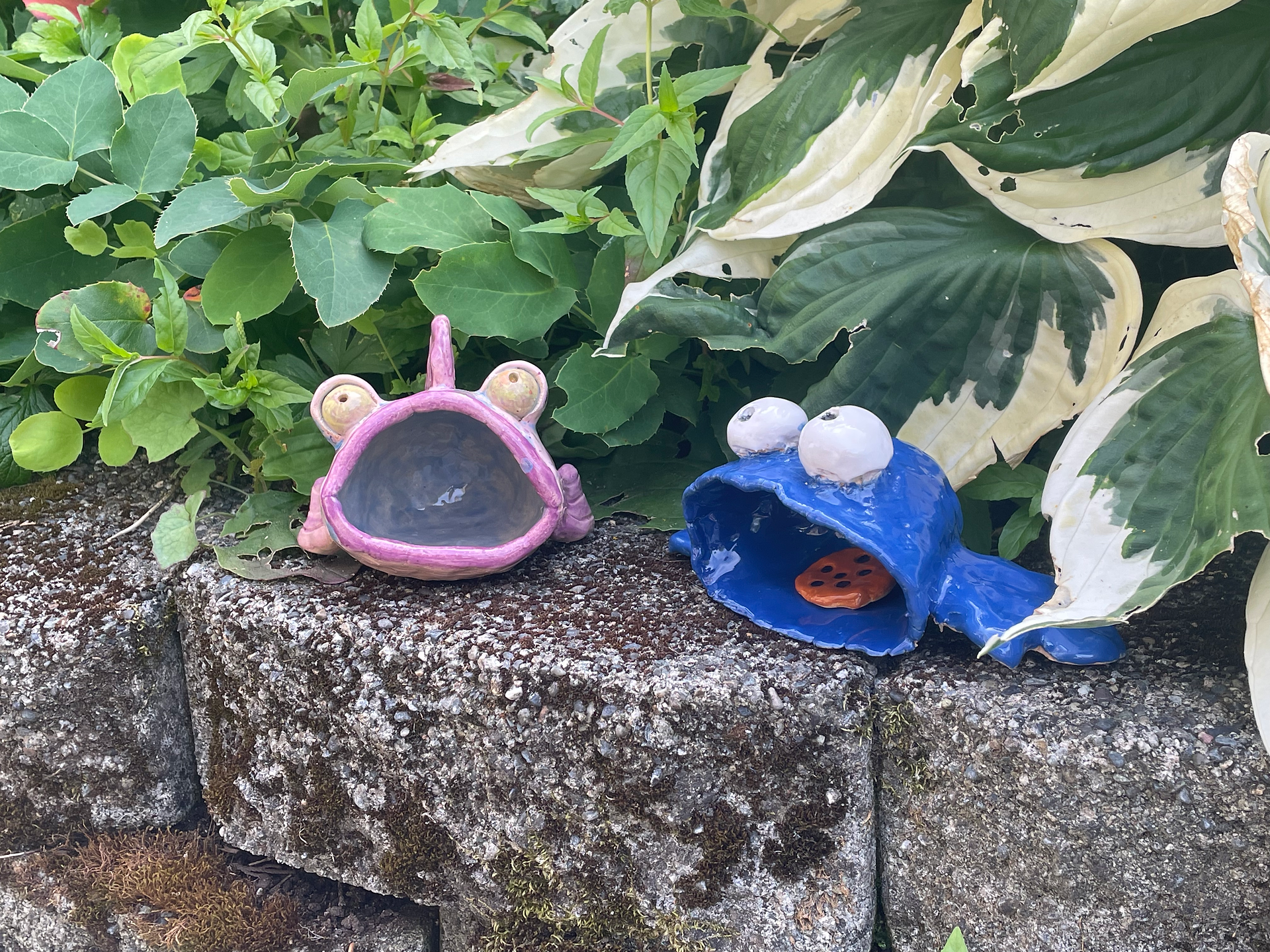 Pink fish and blue Cookie Monster on stone ledge with hasta behind