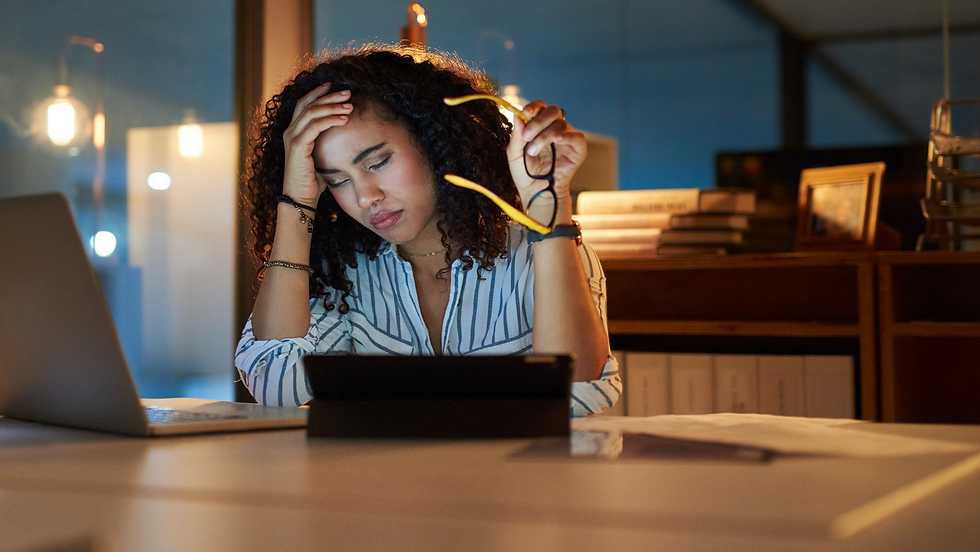 Giovane donna seduta in ufficio alla sera, con espressione stanca e occhi chiusi, mentre tiene in mano gli occhiali. L’immagine trasmette disallineamento interiore e affaticamento emotivo legati all’esperienza lavorativa.