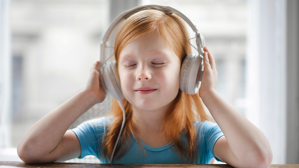Bimba che ascolta un paio di grandi cuffie audio, con occhi chiusi. La scena trasmette fiducia e contatto umano. Luci soffuse, atmosfera intima.