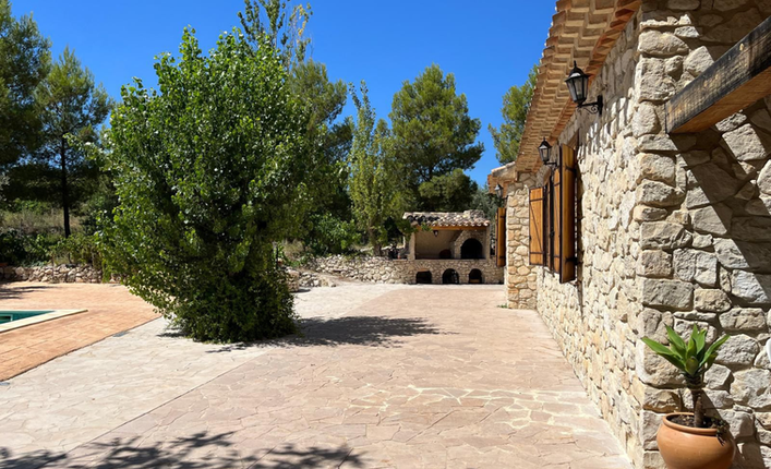 Stone facade of Andalusian country house with outdoor barbecue area and trees under blue sky in Vélez-Blanco.