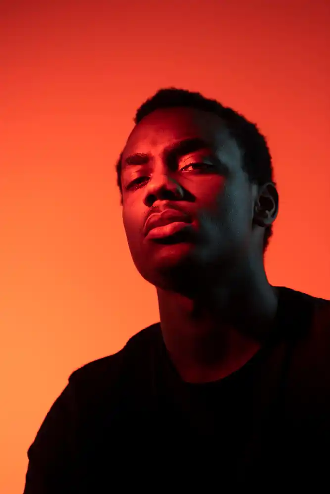 Serious man in black shirt, dramatically lit by red light.