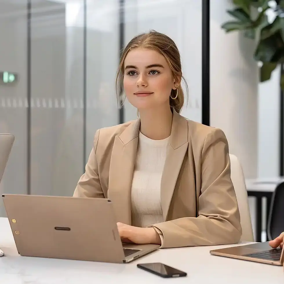 Young woman in beige blazer working on laptop in office.