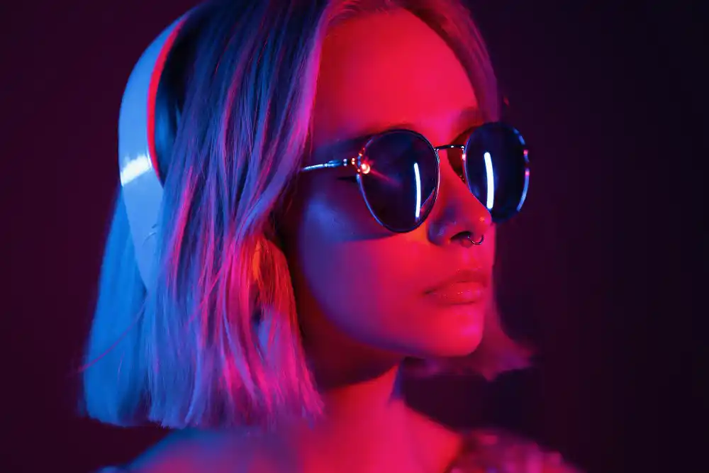 Young woman wearing sunglasses, headphones, illuminated by red and blue neon light.