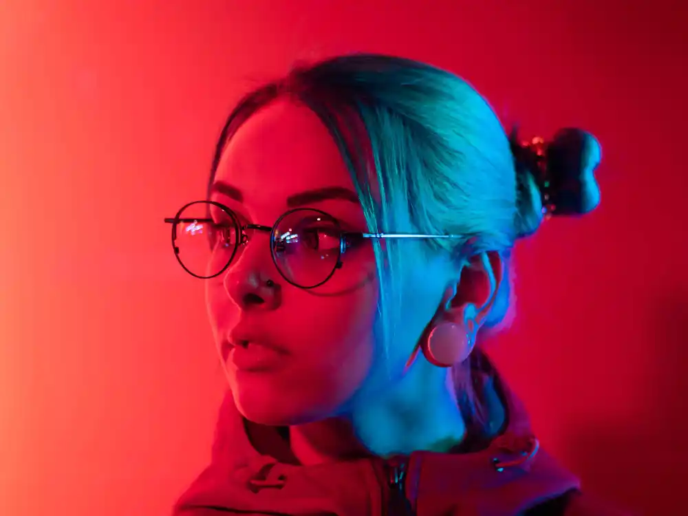 Young woman in glasses, illuminated by vibrant red and blue light.