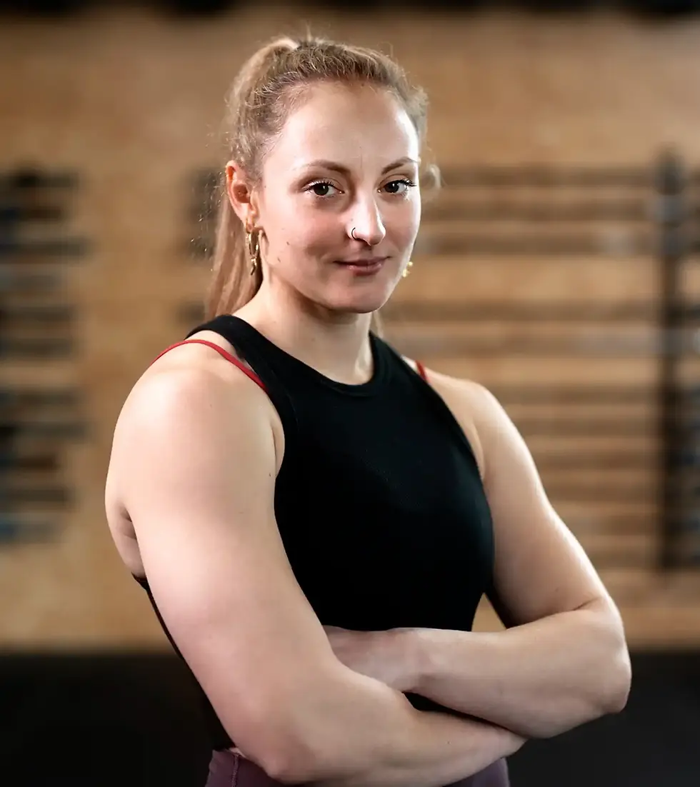 Woman with arms crossed, smiling, wearing black top, at the gym.