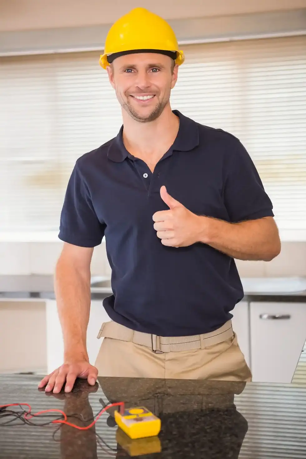 Smiling electrician in yellow hard hat giving thumbs up, about electrical work.