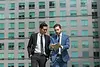Two businessmen in suits review documents together near a tall building.