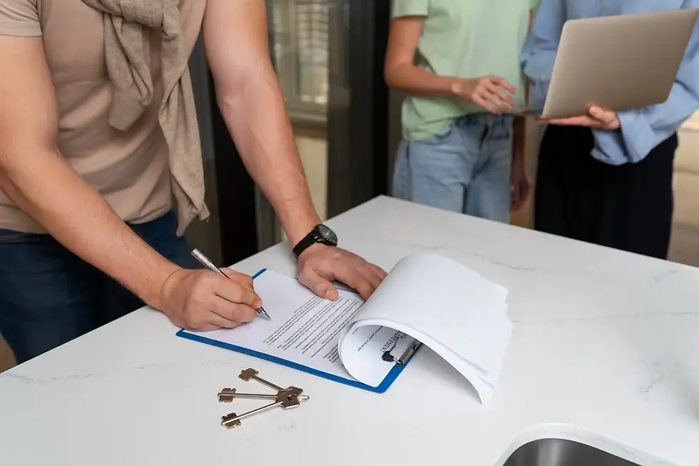 Person signing a contract, keys on the table, with two other people present.
