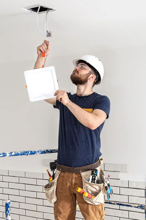 Electrician inspecting wires in ceiling, holding a tablet for project details.