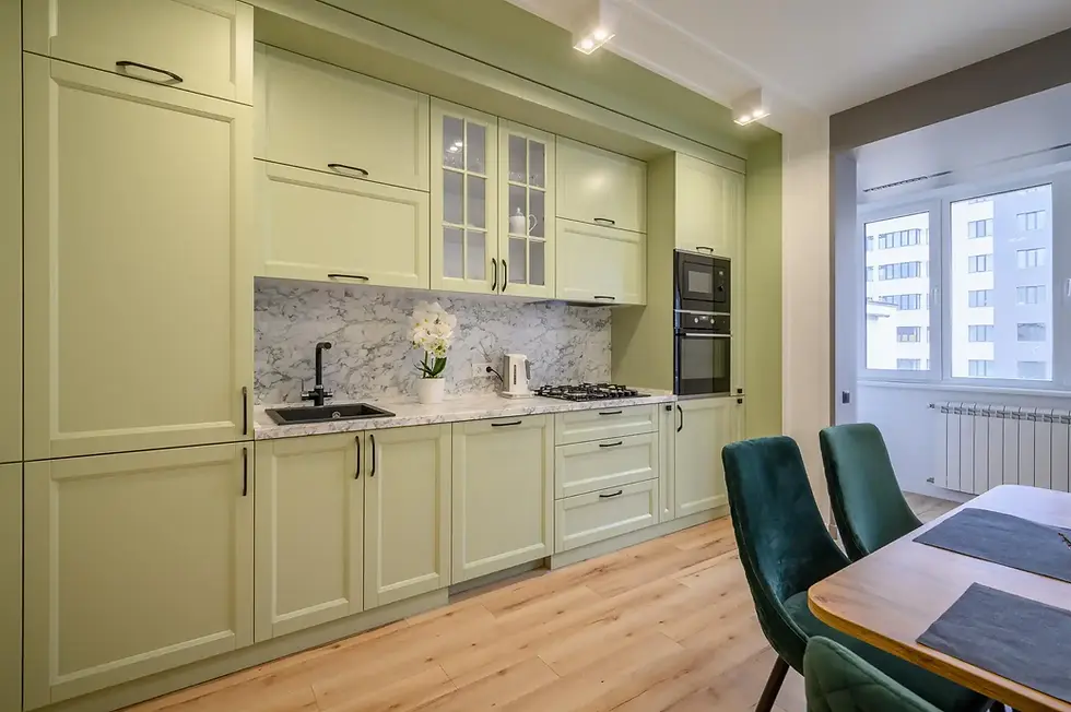 Green kitchen interior with cabinets, stove, sink, and dining table, modern design.