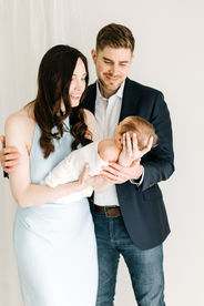 Newborn session in Guelph, Ontario capturing parents smiling at swaddled baby in a soft, neutral studio setting