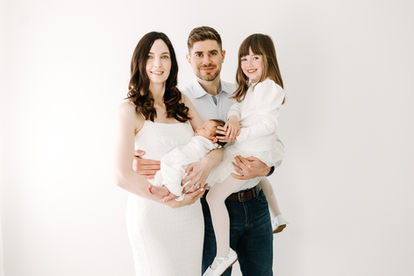 Newborn session in Guelph, Ontario featuring family portrait with newborn baby wrapped in white and sibling standing beside parents in neutral outfits