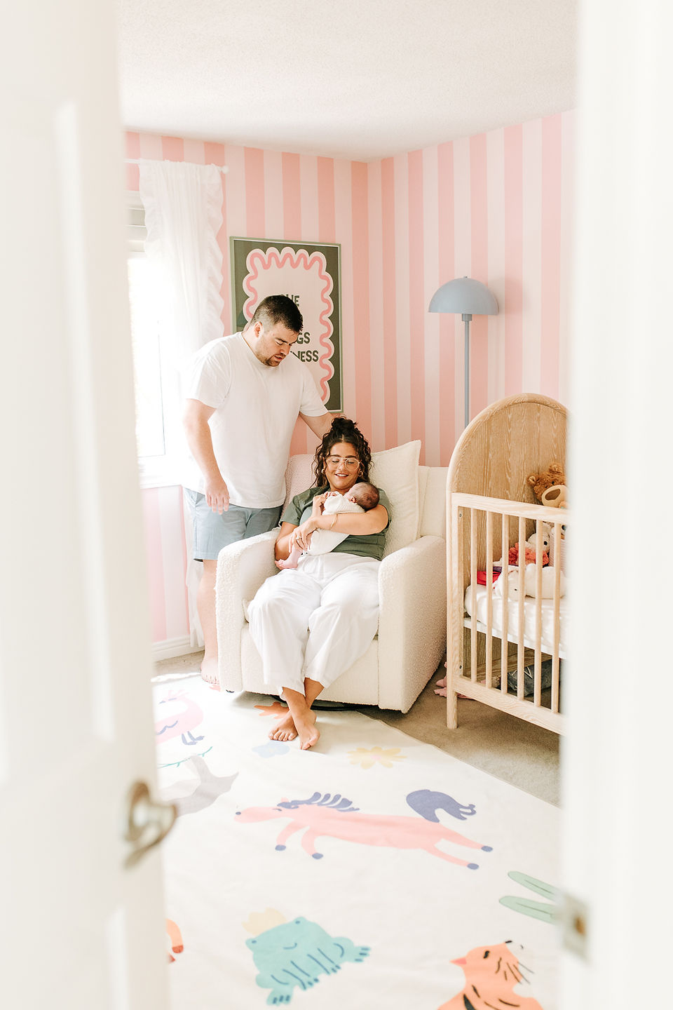 Newborn photography in Guelph, Ontario capturing parents and baby in a nursery with dad's hand-painted striped wallpaper
