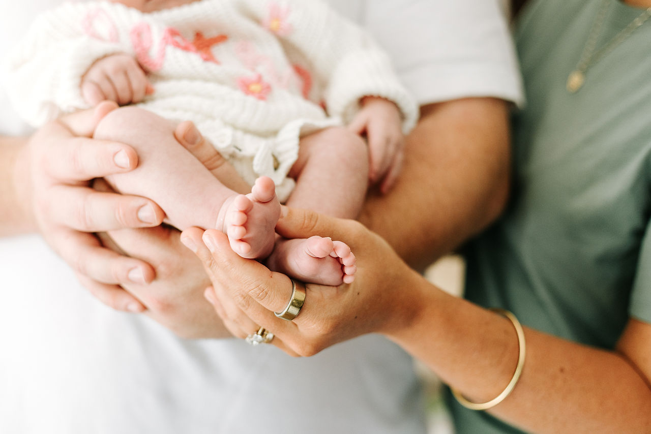 In-home newborn session in Guelph, Ontario featuring a close-up of newborn baby's tiny feet gently held by mom and dad.