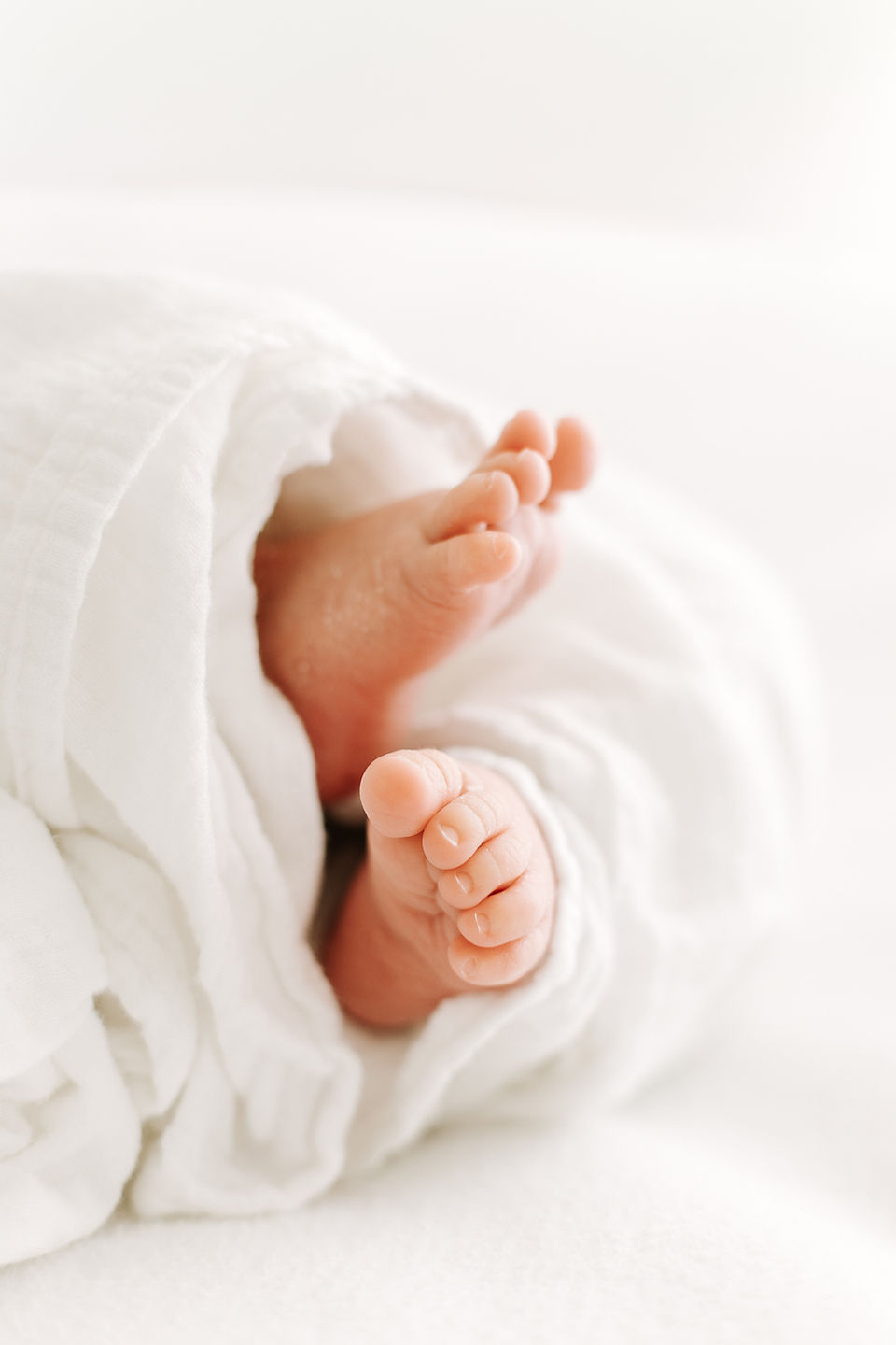 Tiny newborn baby feet during a newborn session in Guelph, Ontario wrapped in a white blanket with soft natural lighting