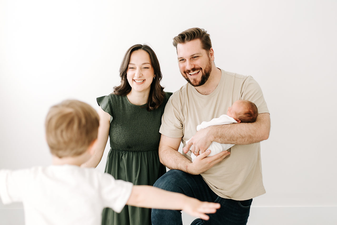 Newborn session in Guelph, Ontario featuring family of four in a soft, bright studio setting with a swaddled baby and sibling interaction