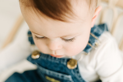 First bite of cake in the first birthday cake smash session in classic jean overall oufit