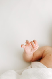 Newborn session in Guelph, Ontario featuring close-up detail of baby hand wrapped in white blanket in a soft, minimal studio setting