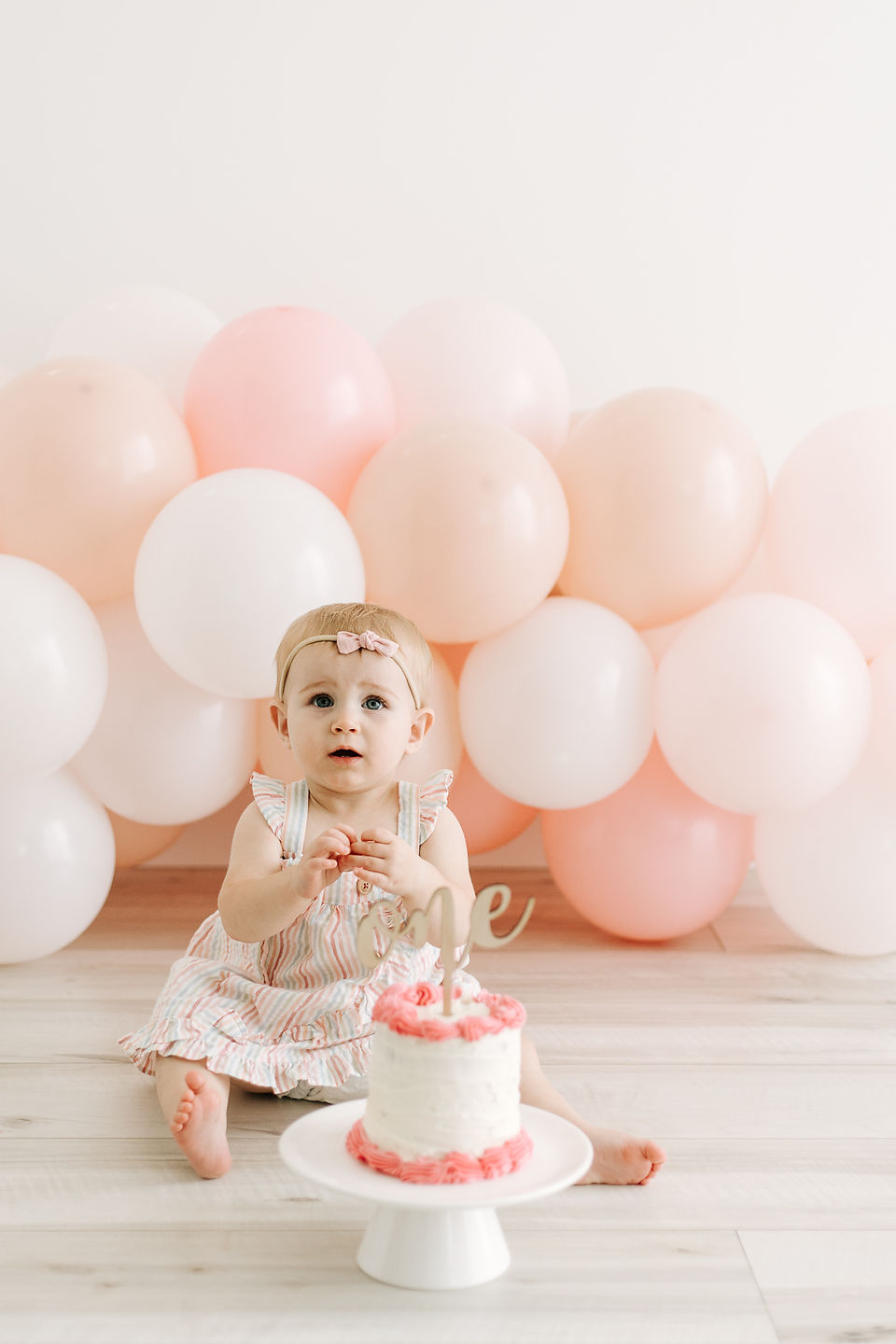 Baby girl celebrating her first birthday with a cake smash session in Guelph, Ontario, surrounded by pastel pink, peach, and white balloons.