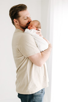 Father kissing sleeping newborn baby during a newborn session in Guelph, Ontario in a bright, minimalist studio setting