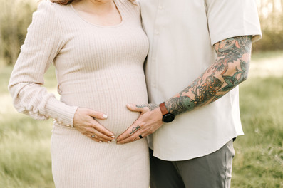 Maternity session in Guelph, Ontario featuring expecting parents embracing in a grassy field with hands on baby bump