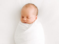Newborn baby peacefully sleeping during a newborn session in Guelph, Ontario wrapped in a white blanket against a clean white background
