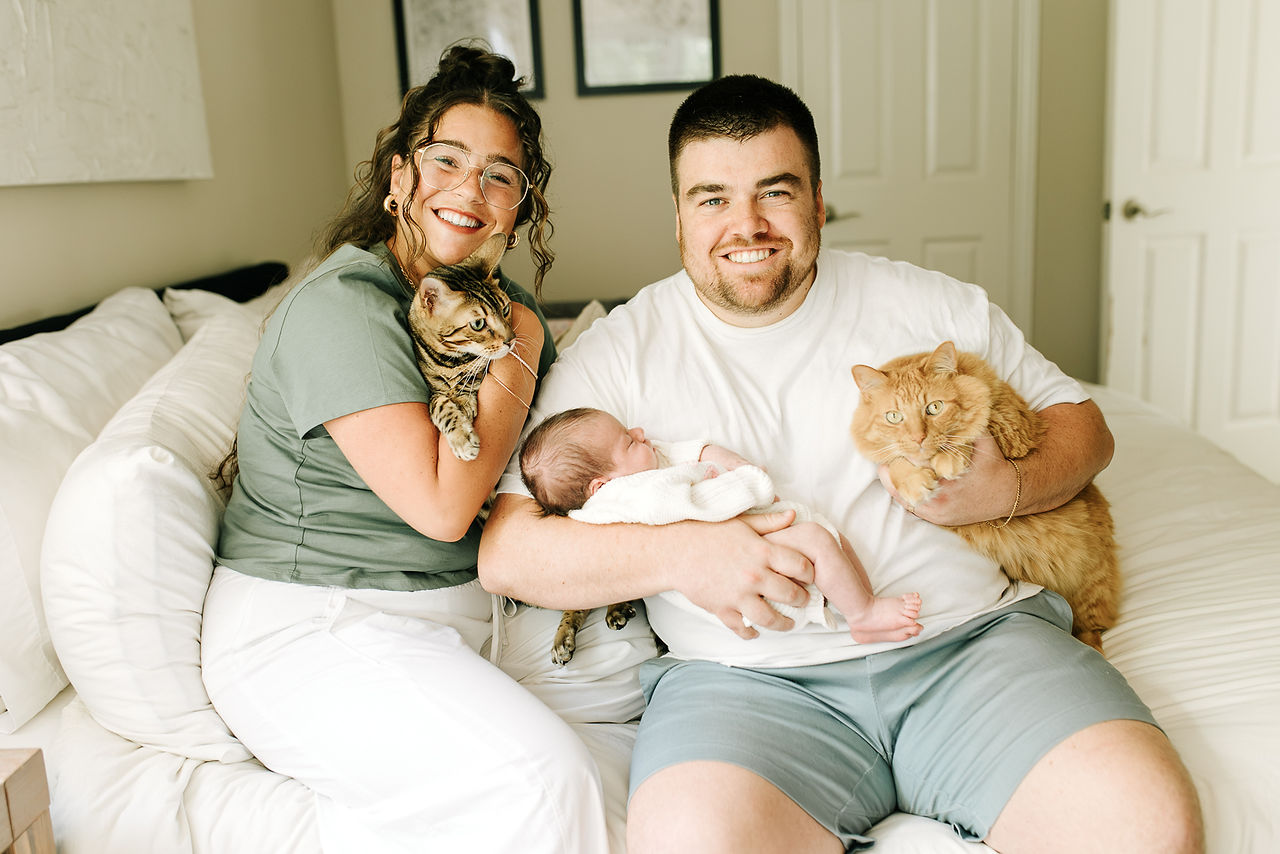 Newborn family photography in Guelph, Ontario capturing parents cuddling their newborn baby with their two cats at home