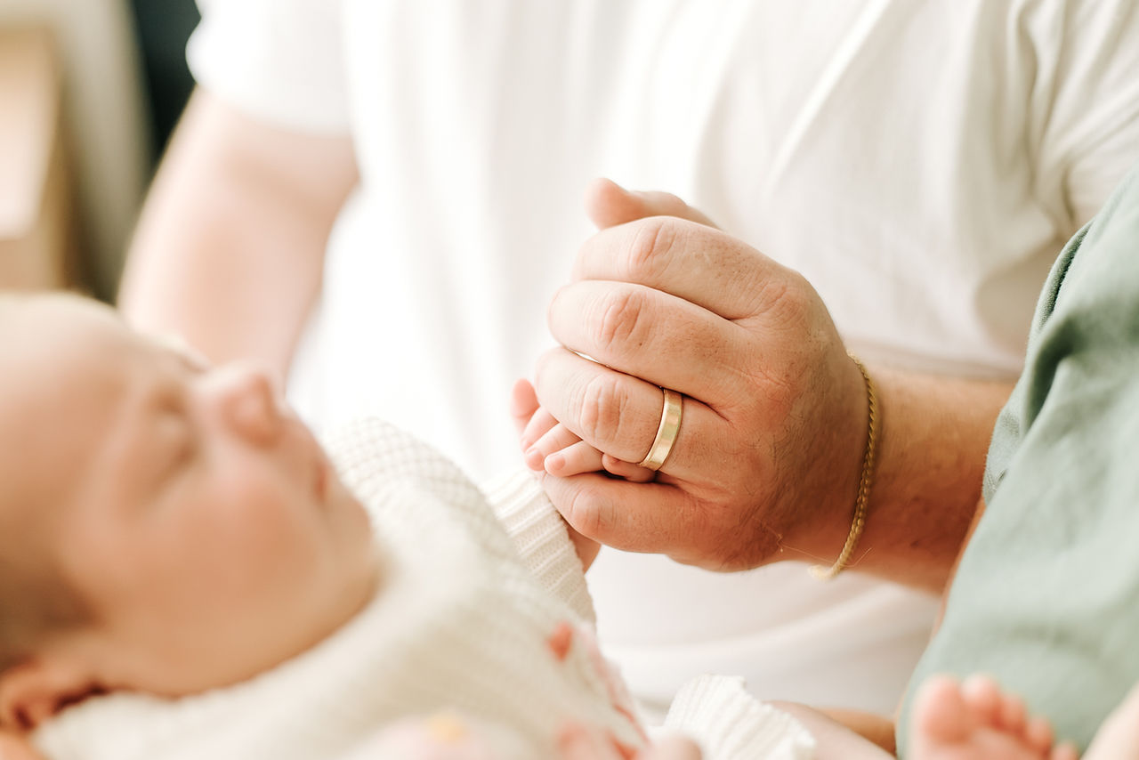 In-home newborn session in Guelph, Ontario featuring a close-up of a dad's hand gently holding their newborn baby's tiny hand