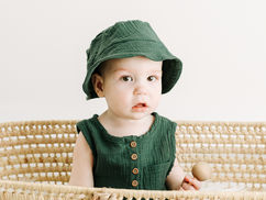 Milestone session in Guelph, Ontario featuring a child in green outfit and bucket hat sitting in a woven basket against a soft neutral backdrop